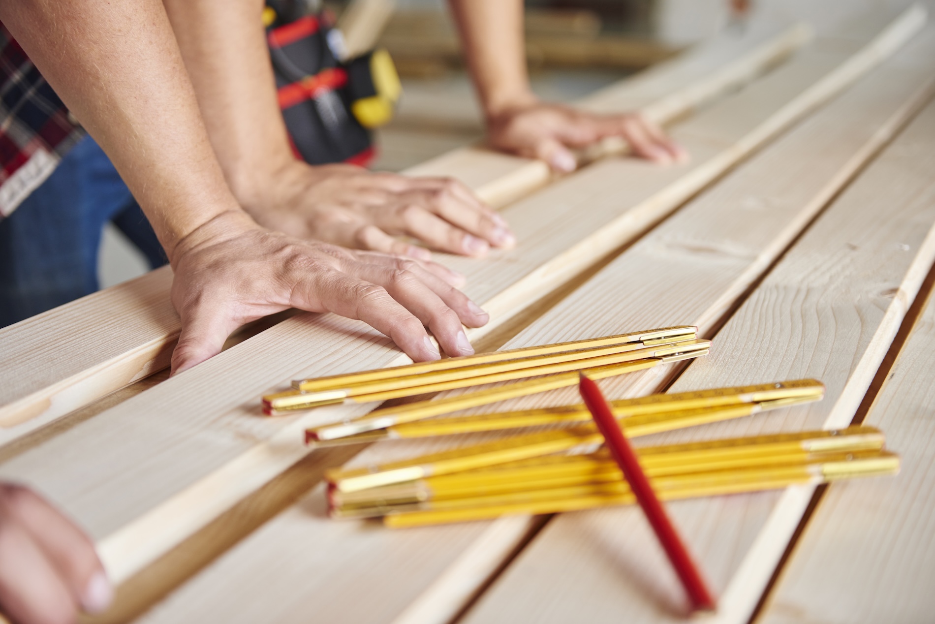 Carpenters measuring wood planks with folding rulers while estimating ADU construction costs